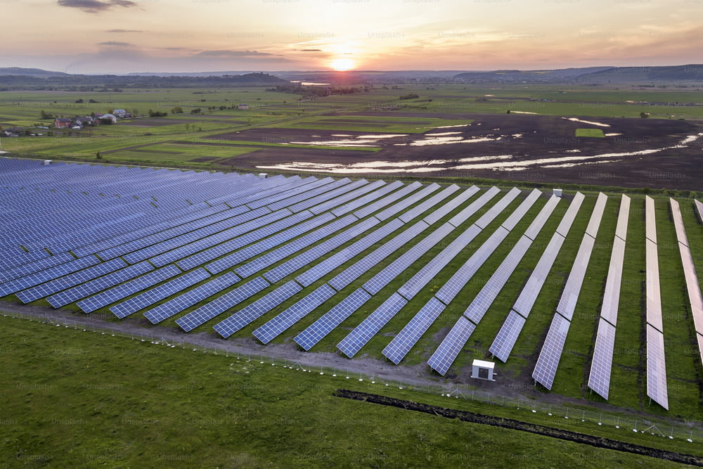 Blue solar photo voltaic panels system producing renewable clean energy on rural landscape and setting sun background.