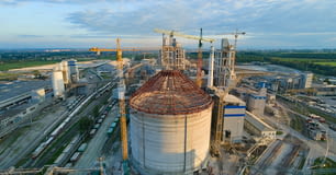 Aerial view of cement factory under construction with high concrete plant structure and tower cranes at industrial production area. Manufacture and global industry concept.