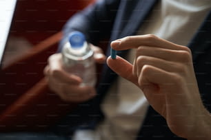 Person, die Medikamente in blauer Pille zwischen den Fingern hält, mit Wasserflasche in der anderen Hand