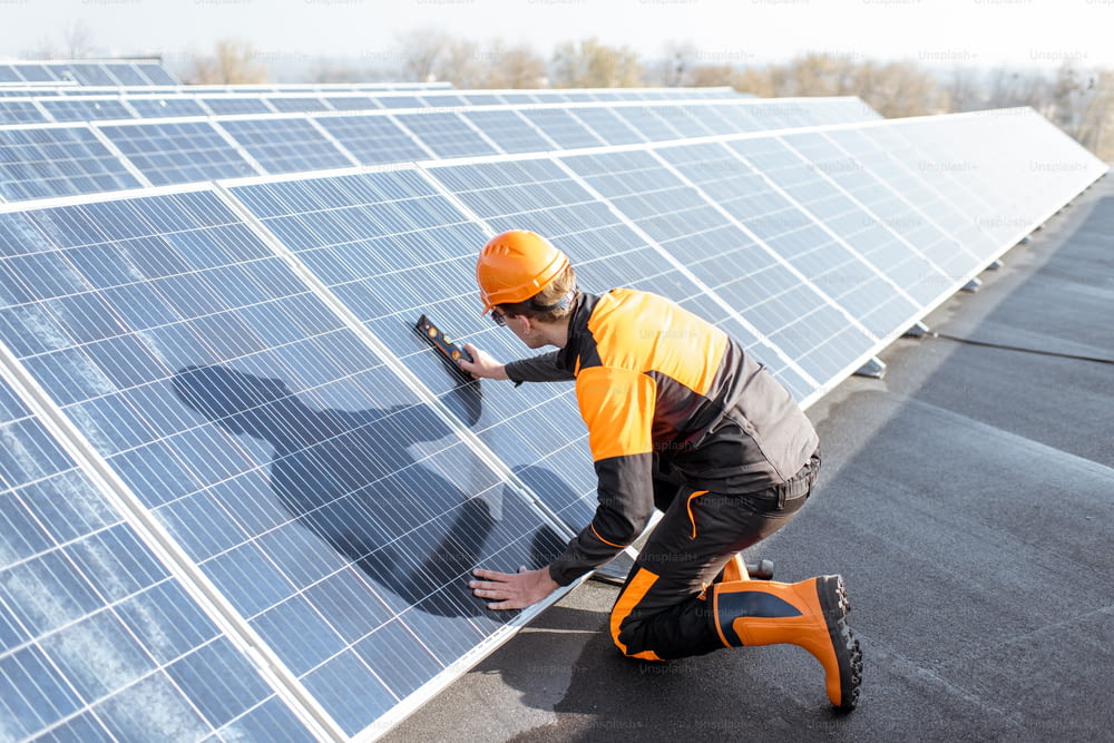 Well-equipped worker in protective orange clothing installing solar panels, measuring the angle of inclination on a photovoltaic rooftop plant