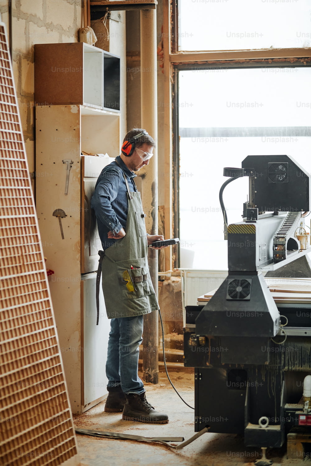 Retrato de cuerpo entero de carpintero que opera una máquina de corte de madera en un taller de producción automatizado