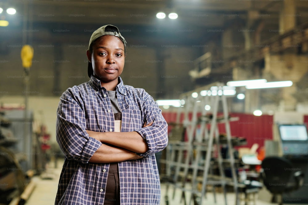 Portrait of female worker posing confidently while standing with arms crossed in factory workshop