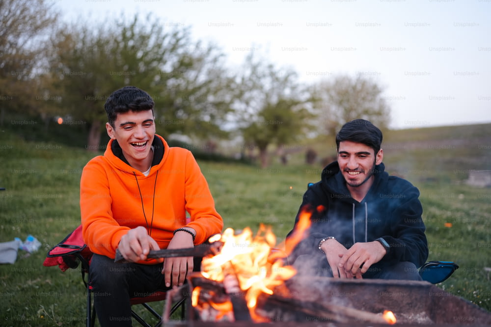 a couple of men sitting next to a fire