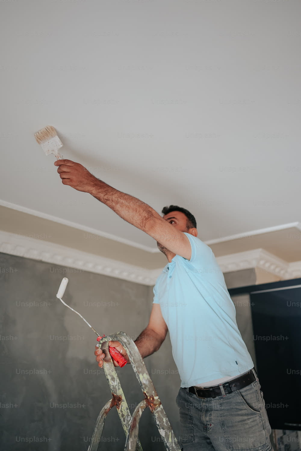 a man is painting a ceiling with a paint roller