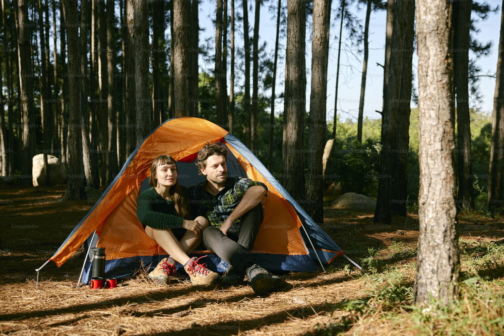 a man and woman sitting in a tent in the woods