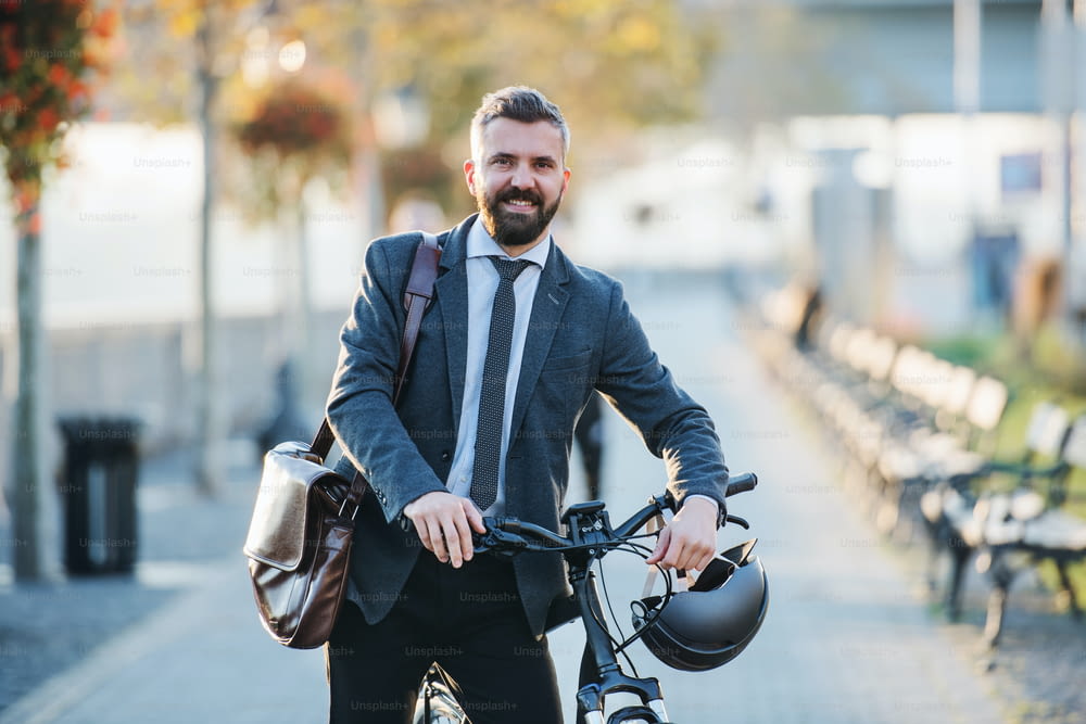 A businessman commuter with bicycle walking home from work in city.