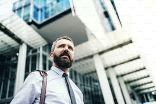 Low angle portrait of businessman standing on the street in city in front of a building. Copy space.