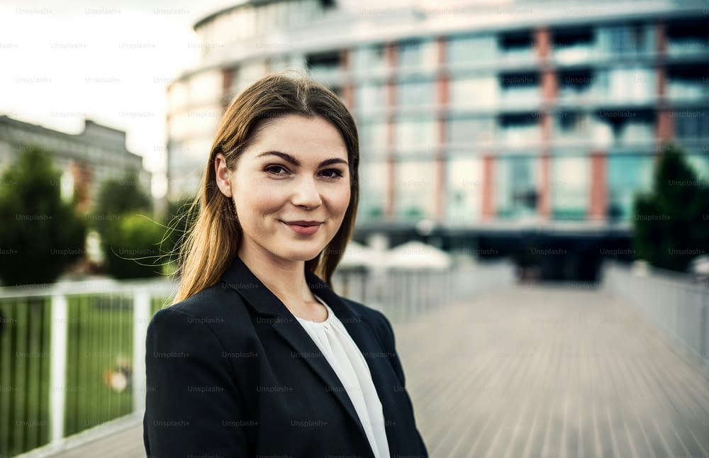 A portrait of a happy young businesswoman standing outdoors in front of a building.