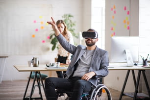Two business people with wheelchair in the office working together. A man wearing VR goggles.