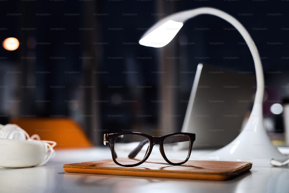 Bureau la nuit avec lunettes, lampe et tablette. L’intérieur de l’espace de bureau de travail.