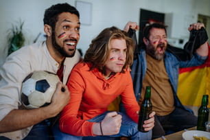 Glückliche deutsche Fußballfans, Freunde, die zu Hause Fußball schauen und Erfolge feiern