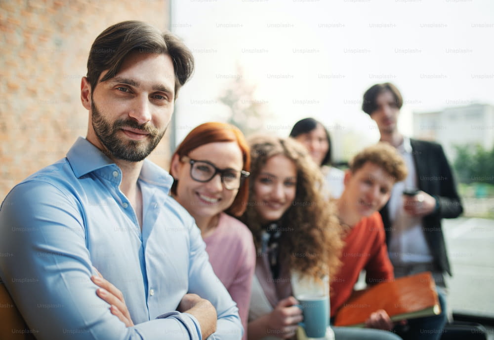 Un ritratto di giovane uomo d'affari con un gruppo di imprenditori al chiuso in ufficio, guardando la macchina fotografica.