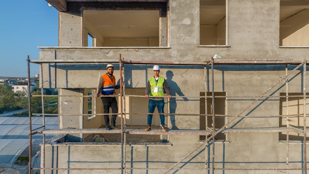 two construction workers standing on scaffolding in front of a building