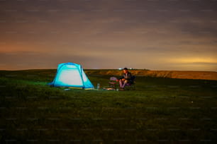 緑豊かな野原の上にあるテントの隣に座っている男性