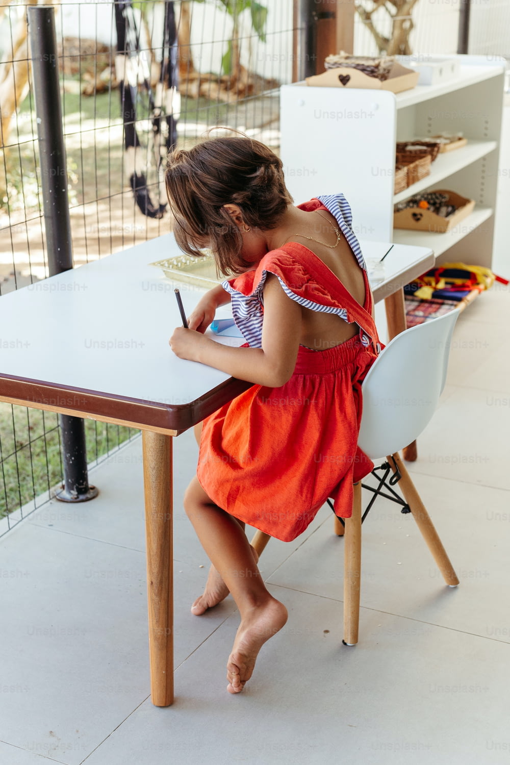 a little girl sitting at a table writing on a piece of paper