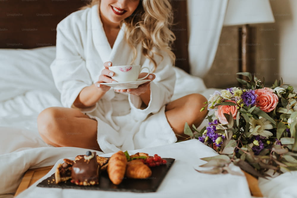 una donna seduta su un letto con in mano una tazza di caffè