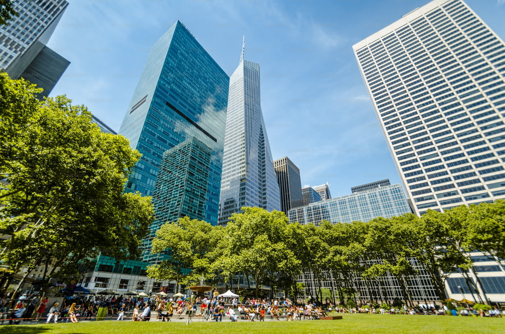 a group of people sitting on a lush green park next to tall buildings