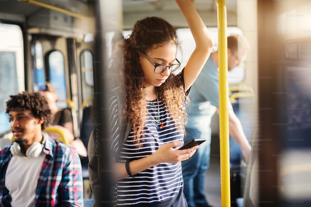 若いかわいい女の子がバスに立って、携帯電話でメッセージをチェックしている。