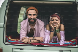 Concetto di stile di vita hippie e viaggi. Ritratto di donna afro-americana allegramente sorridente e maschio hipster che riposa nel bagagliaio posteriore del furgone retrò