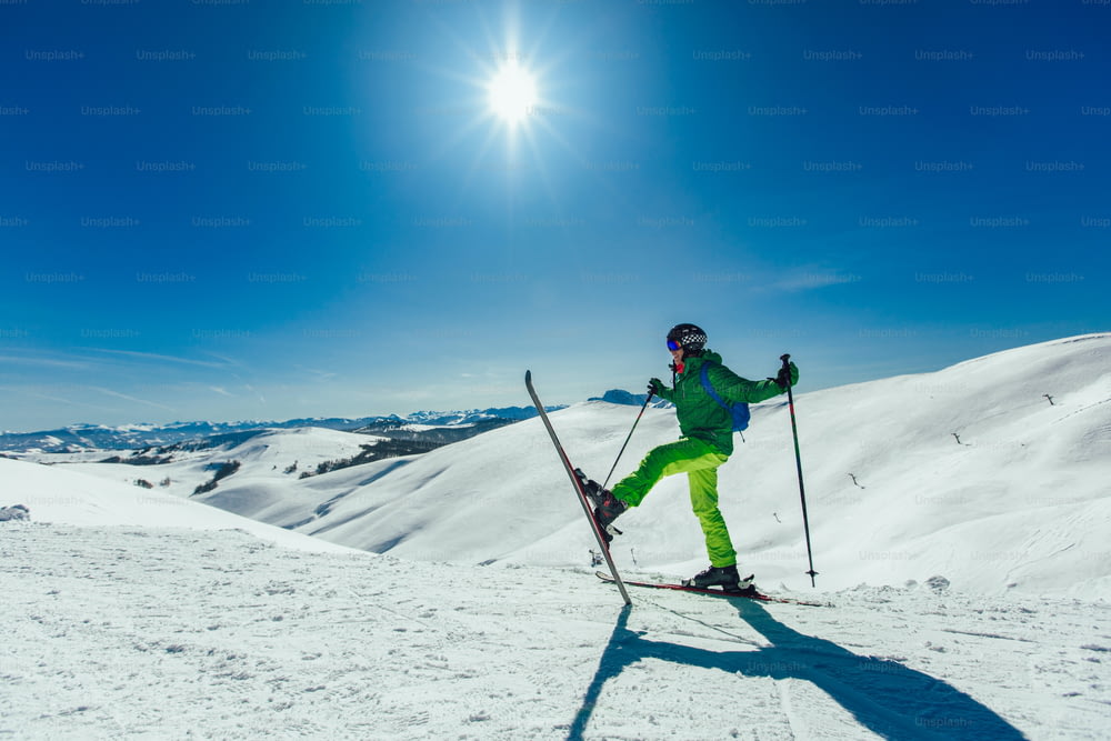 Skifahrer, der an einem sonnigen Tag mit einem erhobenen Bein auf einer Skipiste steht und irgendwo hinschaut