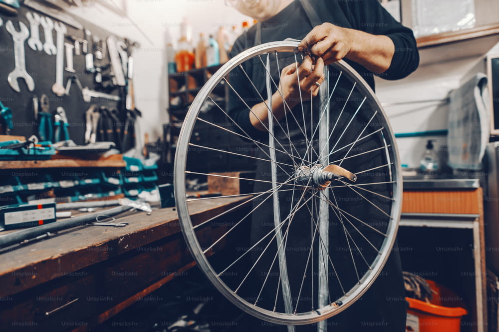 Smiling handsome Caucasian man holding bicycle wheel in hands while standing in workshop.