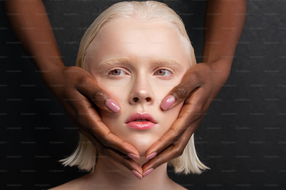 Touching white face. Dark-skinned hands with light pink nails touching white face of her friend