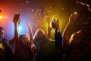 Multitud de jóvenes alegres y despreocupados agitando artilugios con linternas encendidas mientras apoyan a su cantante favorito en el concierto