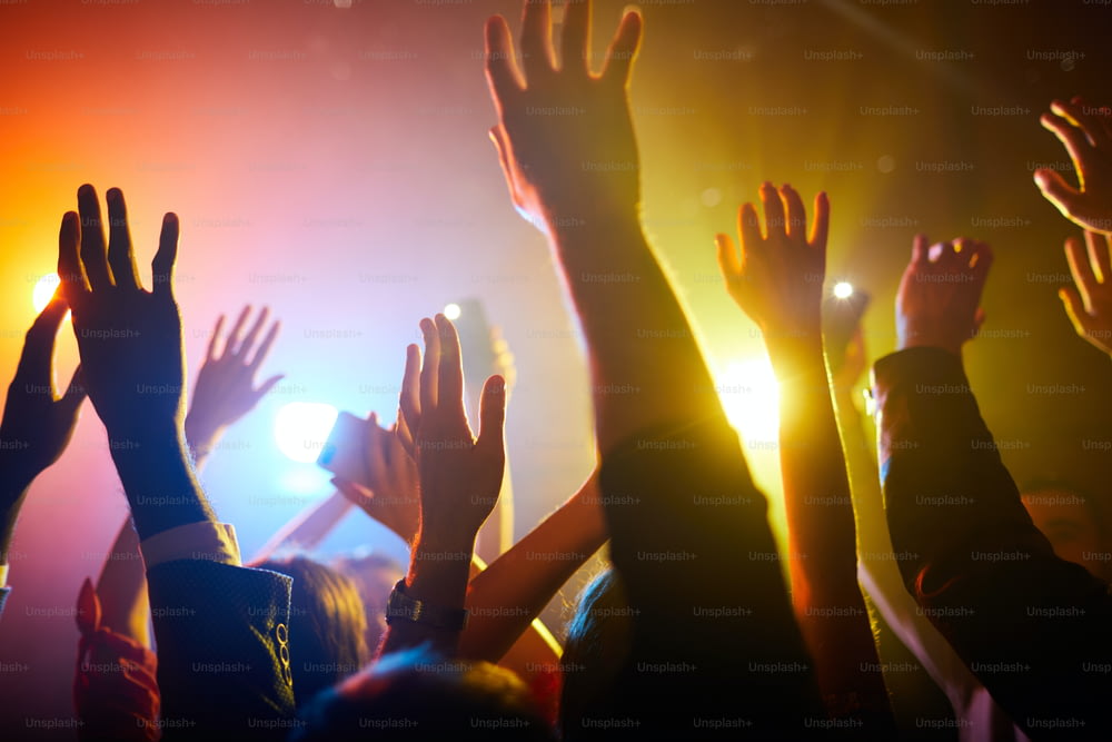 Grupo de personas irreconocibles de pie en una luz colorida y agitando las manos en el aire durante la actuación del músico
