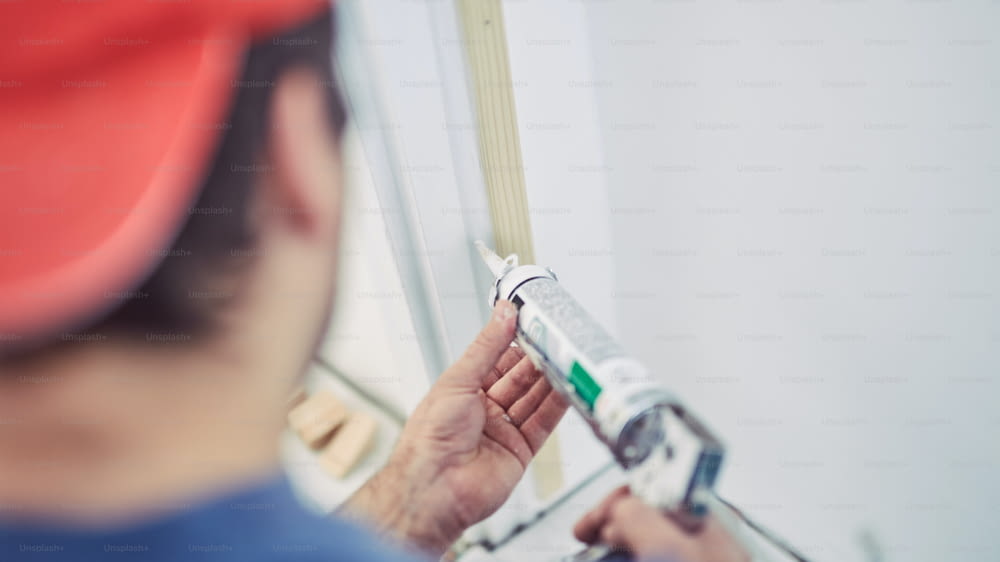 Lavoratore che utilizza silicone per pareti e telaio della porta all'interno della casa - correzioni di ristrutturazione.
