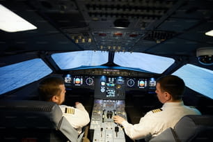 Vista trasera de pilotos serios concentrados en camisas blancas con rayas sentados en el panel de control de la aeronave y preparándose para el vuelo
