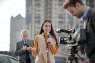 Vivir. Joven y linda reportera con un traje beige hablando con una cámara de video