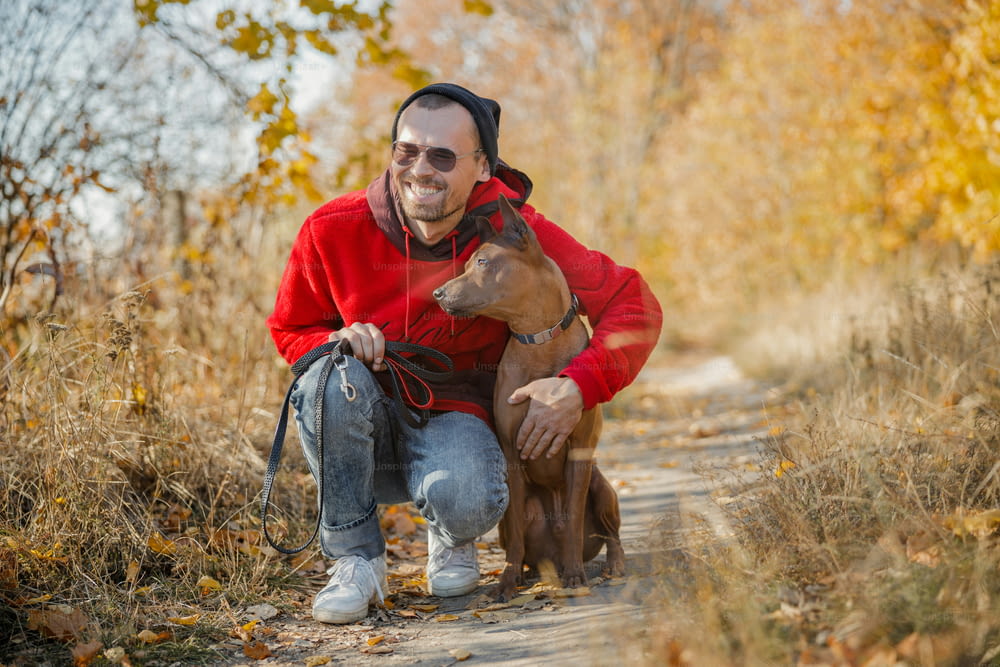 Giovane proprietario positivo che sorride felice mentre abbraccia il suo cane nella foresta