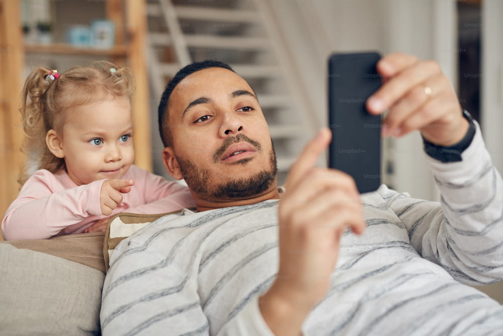Retrato de un padre joven que muestra juegos de teléfonos inteligentes a una linda hija pequeña en casa, espacio de copia