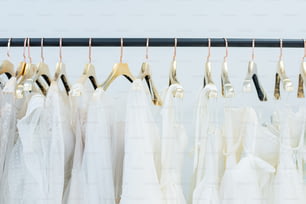 Various white dresses on hangers hanging in row on rack in wedding gown store