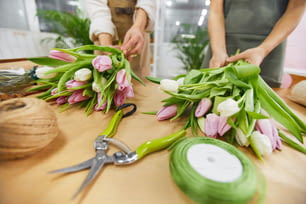 꽃 가게에서 일하는 동안 봄 시즌을 위해 튤립 꽃다발과 꽃 작품을 준비하는 두 명의 알아볼 수 없는 젊은 여성의 클로즈업, 복사 공간