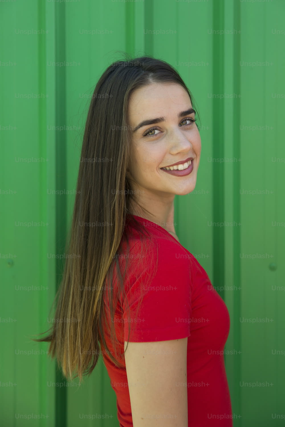 Trendige junge Frau, die an einem heißen Sommertag an der grünen Wand steht