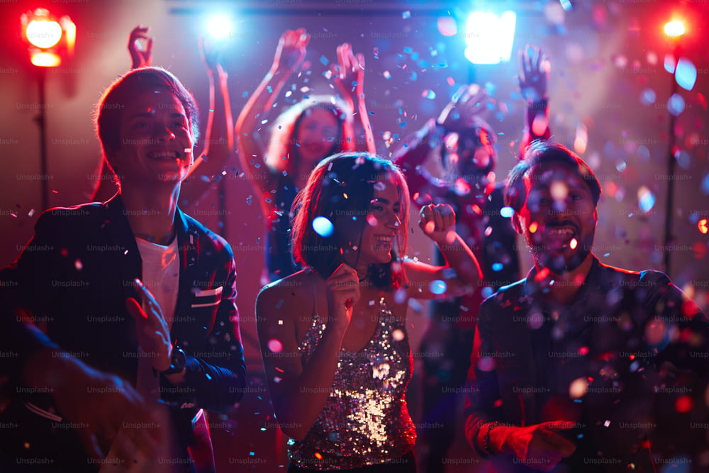 Jóvenes amigos felices bailando en confeti durante la celebración de las vacaciones