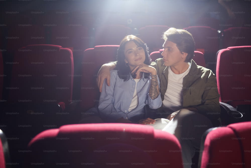 Portrait d’un jeune couple amoureux au cinéma regardant un film tout en profitant d’un rendez-vous, un homme regardant sa petite amie avec affection et l’embrassant, copiez l’espace