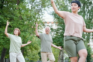 Content senior couple performing slow-flowing movements at group qigong class outdoors