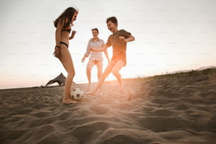 Happy family playing football on the beach having great family time on summer holidays.