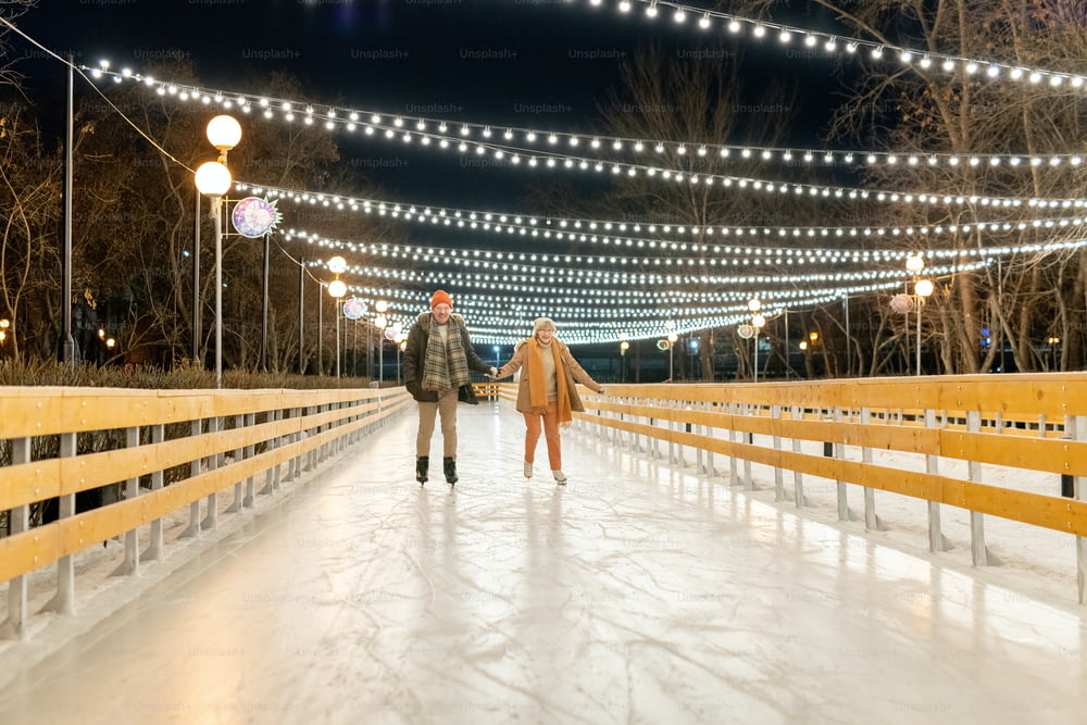 公園のリンクで一緒にスケートをしながら手をつないで幸せな熟女夫婦