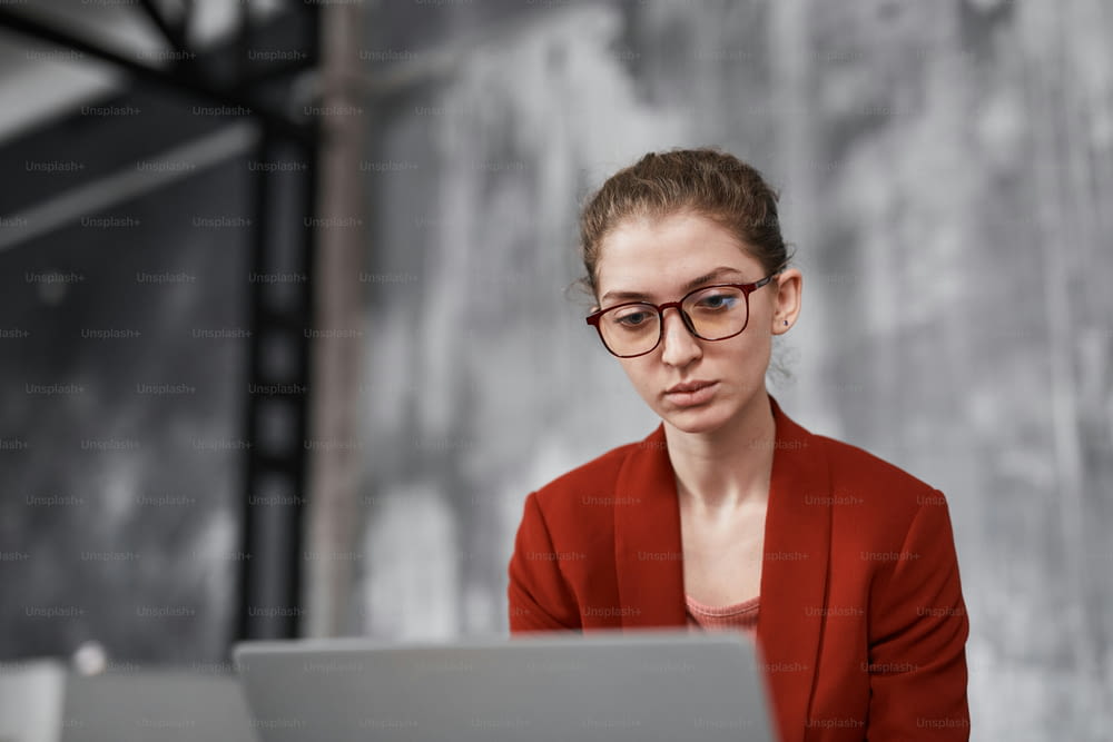 Portrait of young businesswoman wearing red while working against grey wall in office, copy space