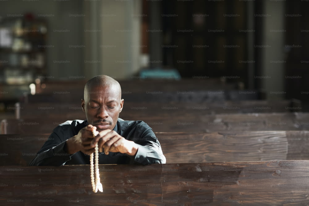 Homem africano sentado na igreja segurando contas e orando com os olhos fechados