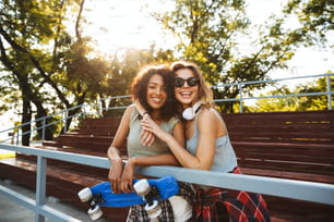 Two cheerful young girls with skateboard having fun together at the park