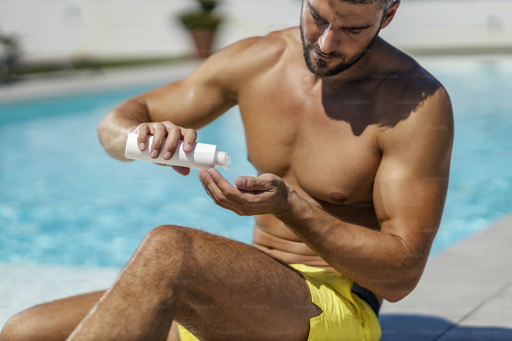 Sun protection, cosmetics, and creams. A sexy man applies sunscreen and sunscreen while sitting by the pool in a bathing suit. Skin protection and skincare from UV radiation, love your skin and body