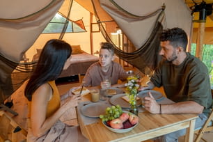 Family of three interacting by served table during breakfast in glamping tent