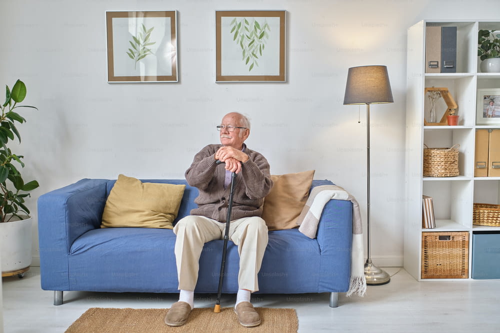 Homme âgé avec béquille assis et reposant sur le canapé dans le salon