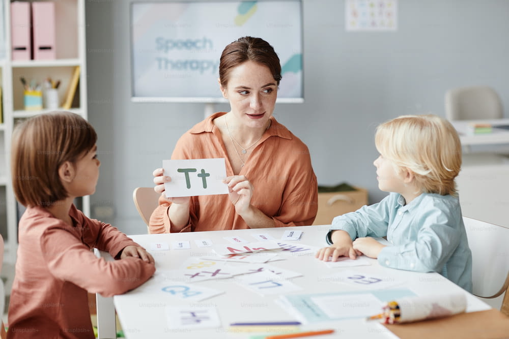 Junge Englischlehrerin, die den Kindern die Karte mit dem Brief zeigt und sie während des Unterrichts am Tisch lernen