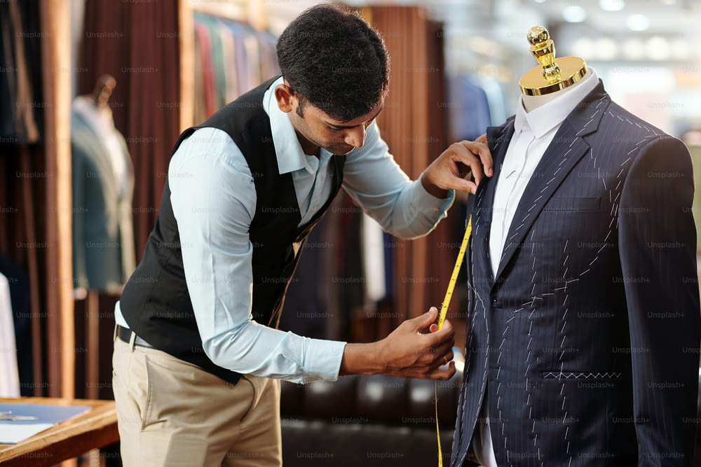 Creative young tailor measuring bespoke jacket on mannequin he is working on