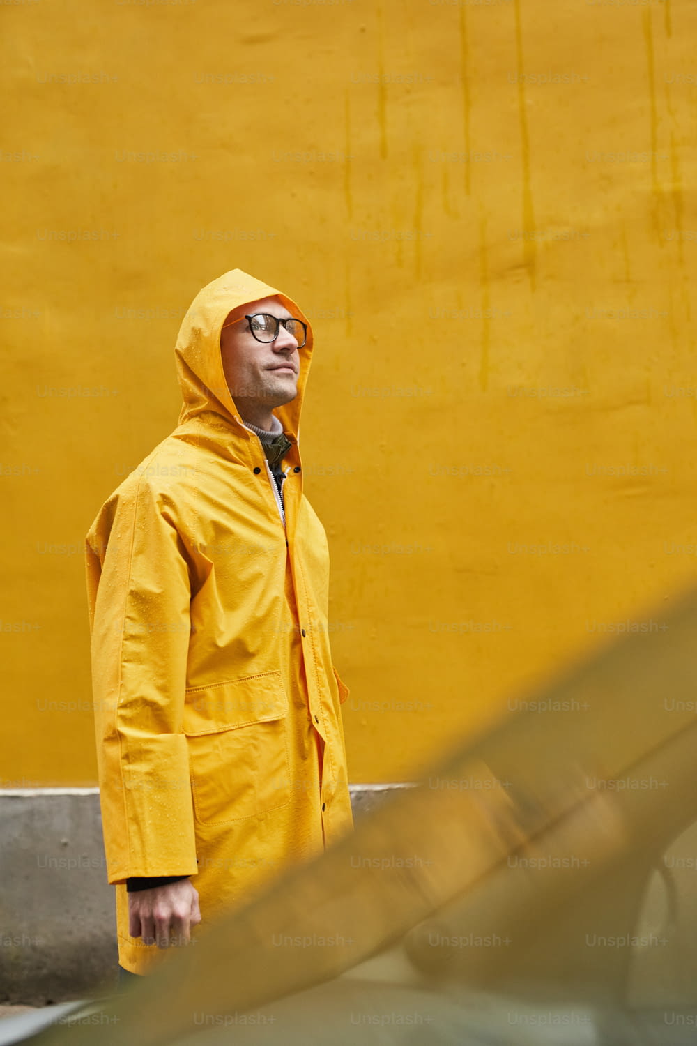 Vertical medium long shot of mature Caucasian man wearing yellow raincoat walking in rain looking away